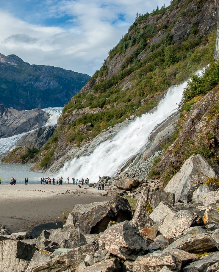 People standing next to body of water and mountains during daytime