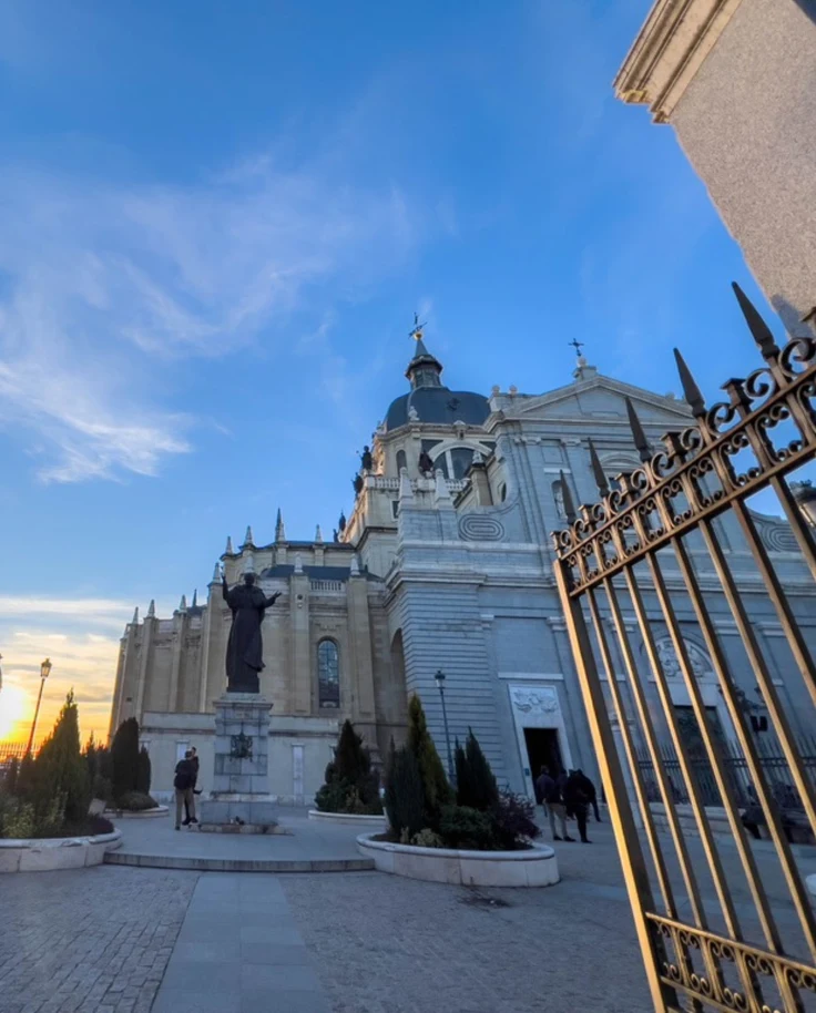 At sunset, An open gate leads to a grand white building with domes under a clear blue sky.