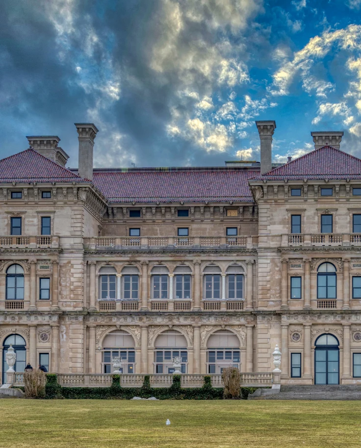 A mansion in Newport, Rhode Island, with a lush lawn in front, and a semi-cloudy sky.