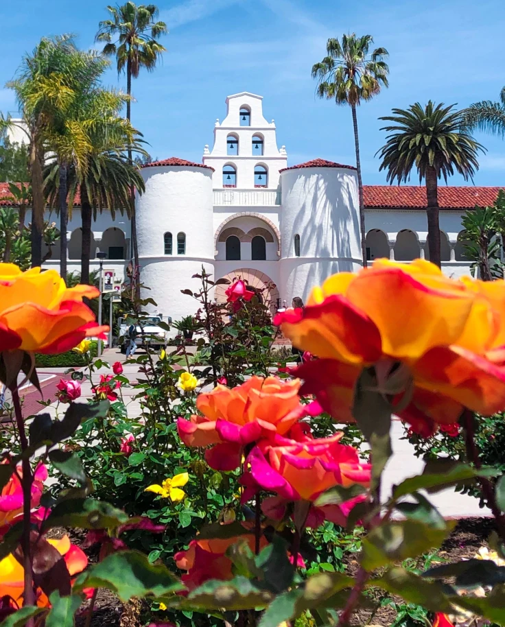 A picture of a white building surrounded with trees and flowers.