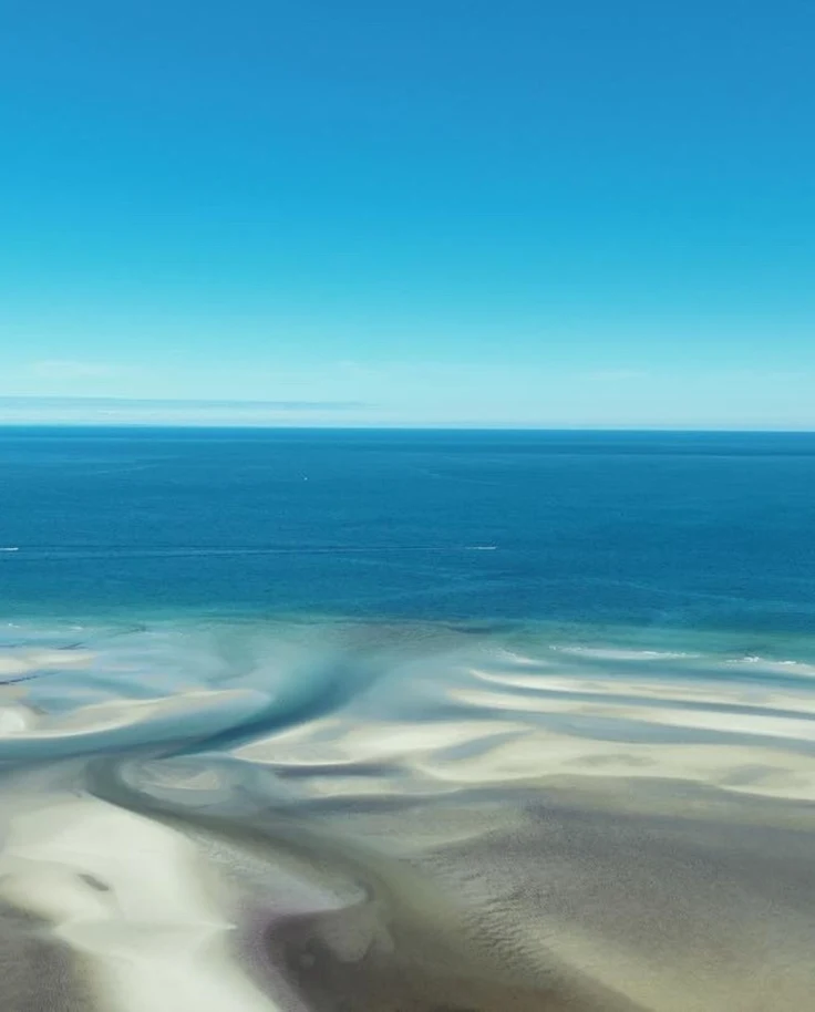 A serene coastal landscape with intricate patterns formed by sand and water channels.