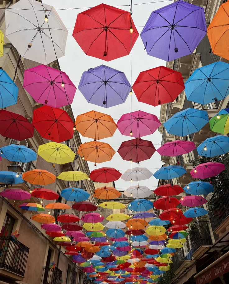 The image displays a vibrant array of colorful umbrellas suspended above a street, creating a festive overhead canopy.