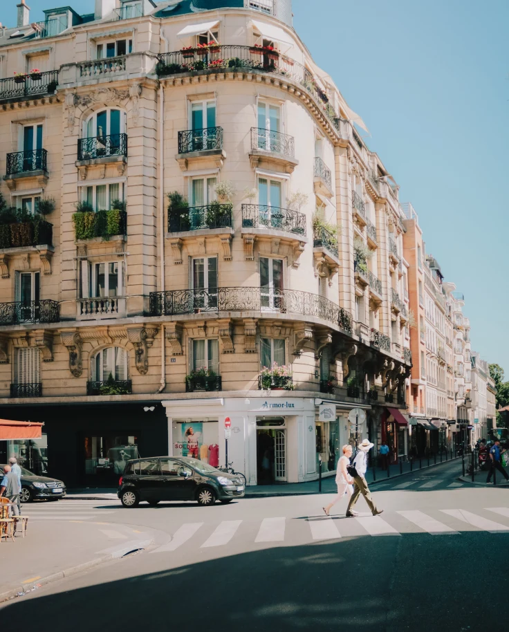 Two people walking on the street next to a tall building on a sunny day