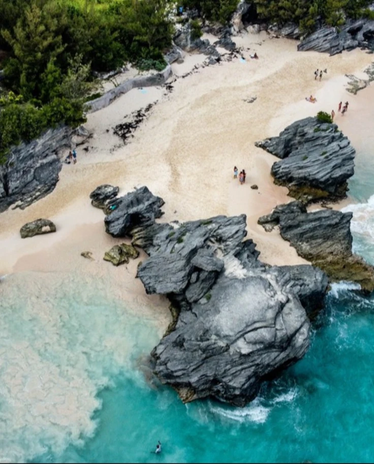 An aerial view of a beach with turquoise waters, large rocks, and people scattered on the sand.