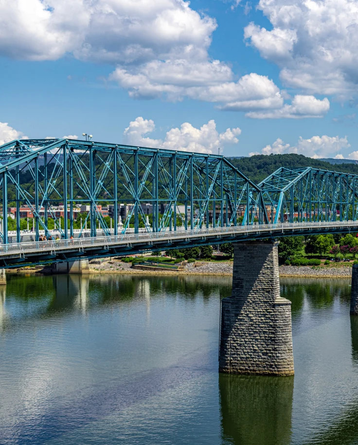 Bridge over blue water in Chattanooga, Tennessee leading to land with green grass and trees on a sunny day