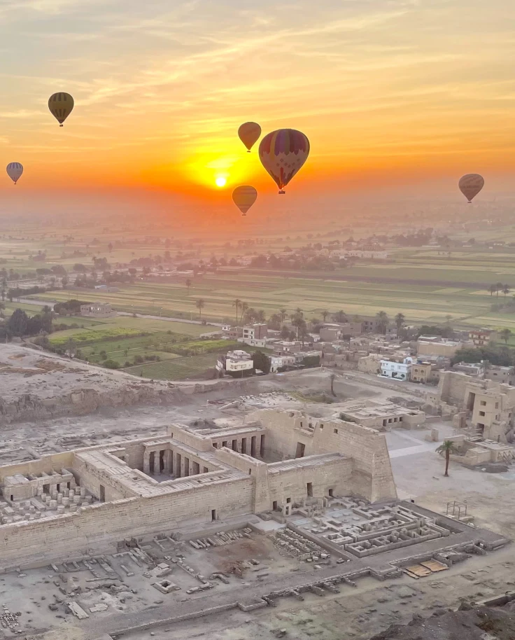 air balloons float in yellow sunrise over ancient desert ruins