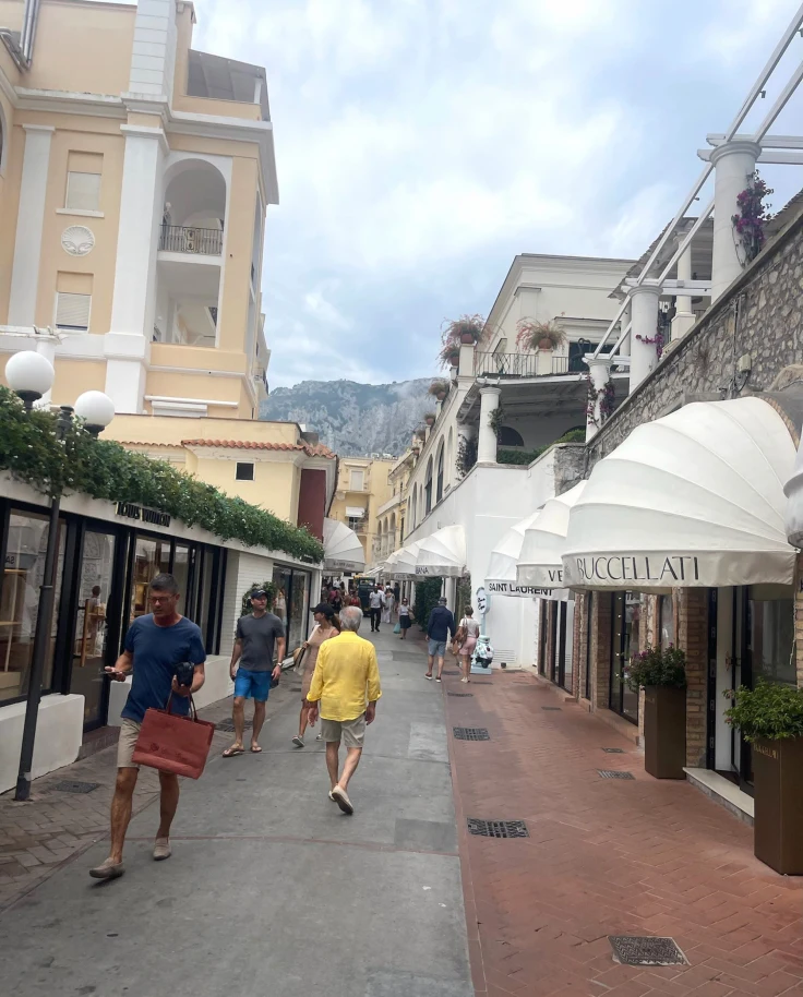 A bustling street scene with pedestrians, shops and buildings under a cloudy sky.
