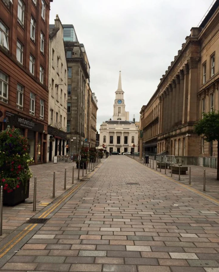 A European city street leading to a white building with a tower in the distance.