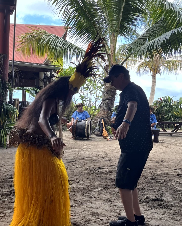 A traditional dancer teaching how to dance to a man on a beach.
