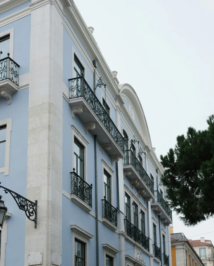 A charming building with blue walls, white trim, and ornate black balconies with arched windows.