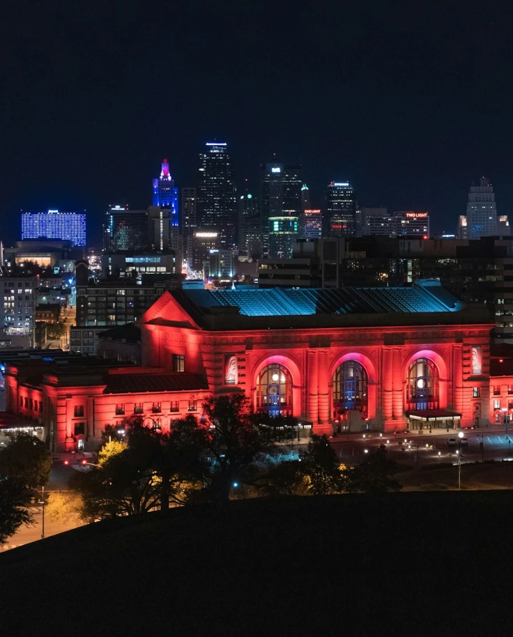 A view of Union Station lit up in red LED lighting in front of a view of the city skyline at nighttime.