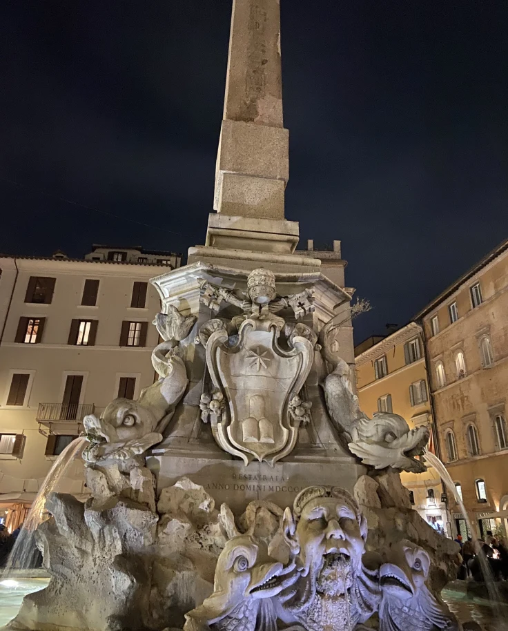 A landmark fountain in the center of a piazza at night,