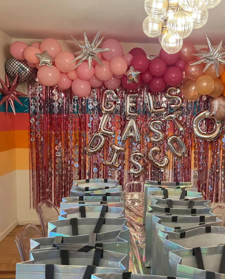 Bachelorette decor complete with gift bags lined up on a table, balloons, streamers and silver signage.