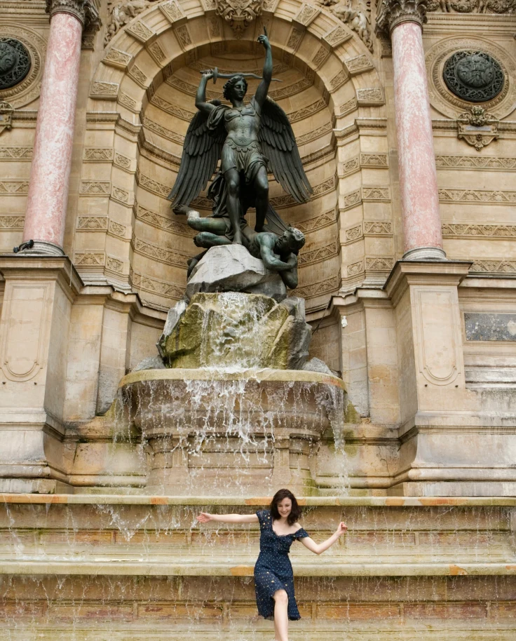 A person stands before a fountain with a statue during the daytime.