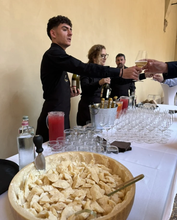 A long table with a large bowl of Parmesan chunks on one end and servers serving drinks.