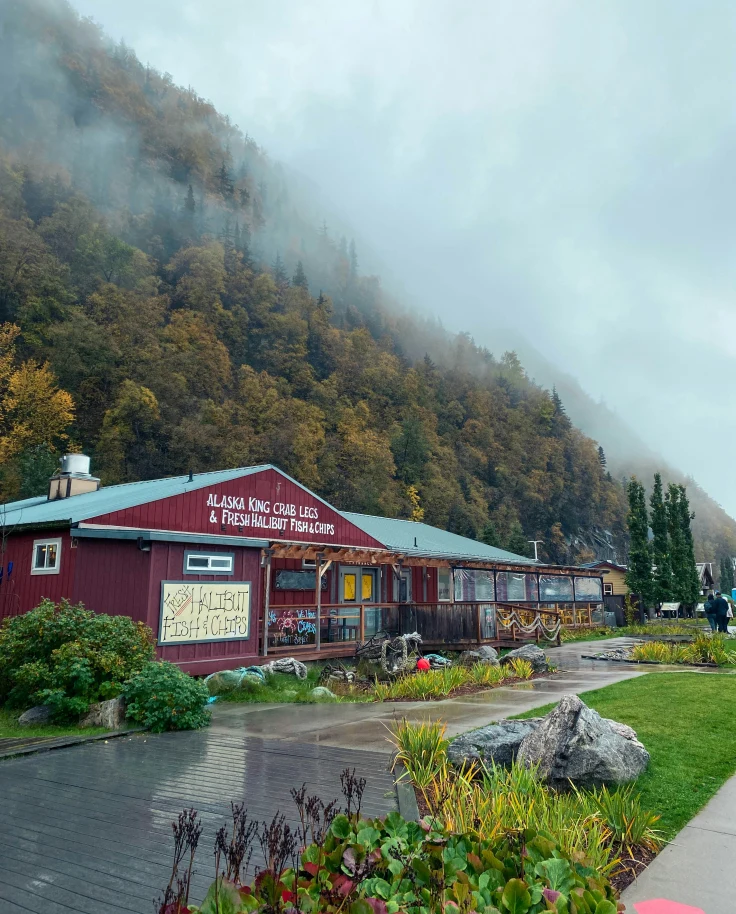 A red building that says "Alaska king crab legs" sitting next to a lush green hillside