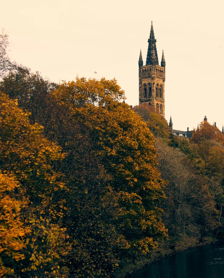 A cathedral spire on a hillside next to a river with trees at sunset in Glasgow.
