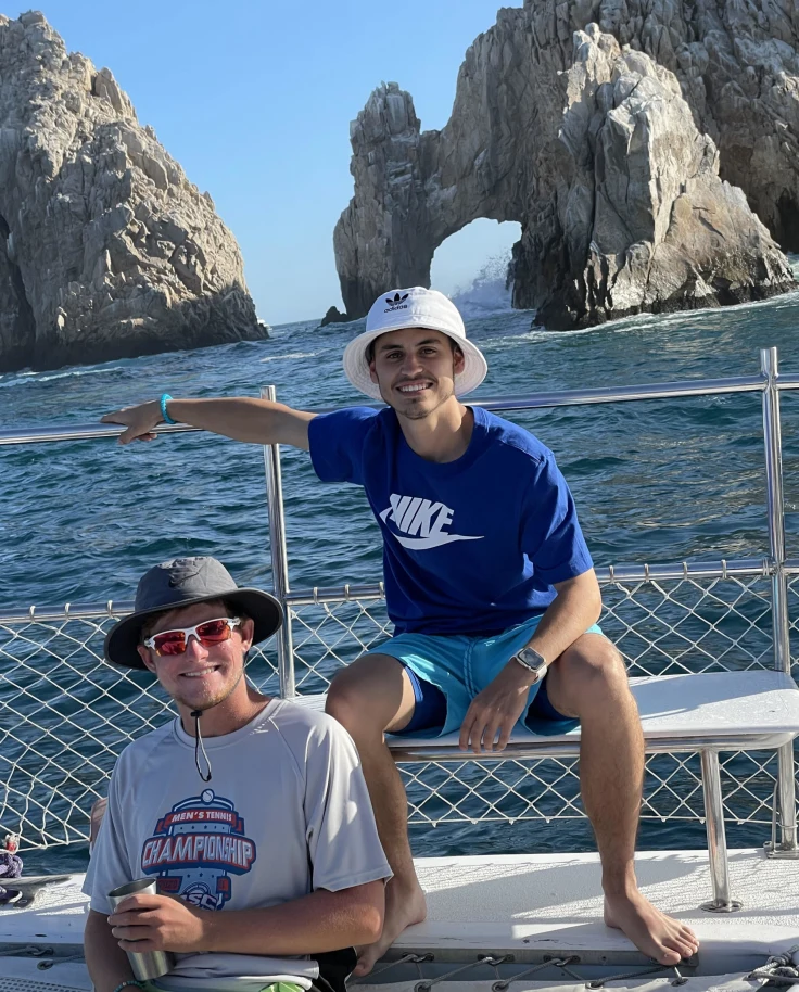 Two individuals on a boat, with rocky formations and the ocean in the backdrop.