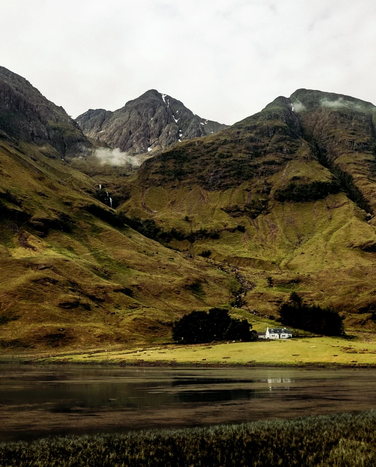 Green pastures with a small house and lake in Scotland.