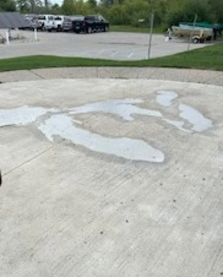 A concrete surface with irregular wet patches, vehicles, and greenery in the background.