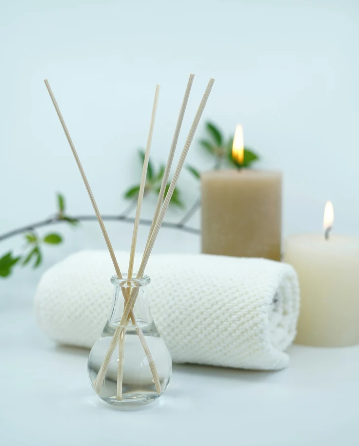 Candles, a white towel and a branch of greenery staged on a table.