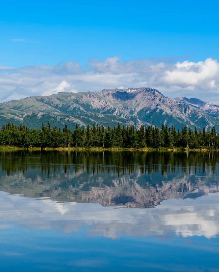 Mountain and trees in front of clear lake reflected.