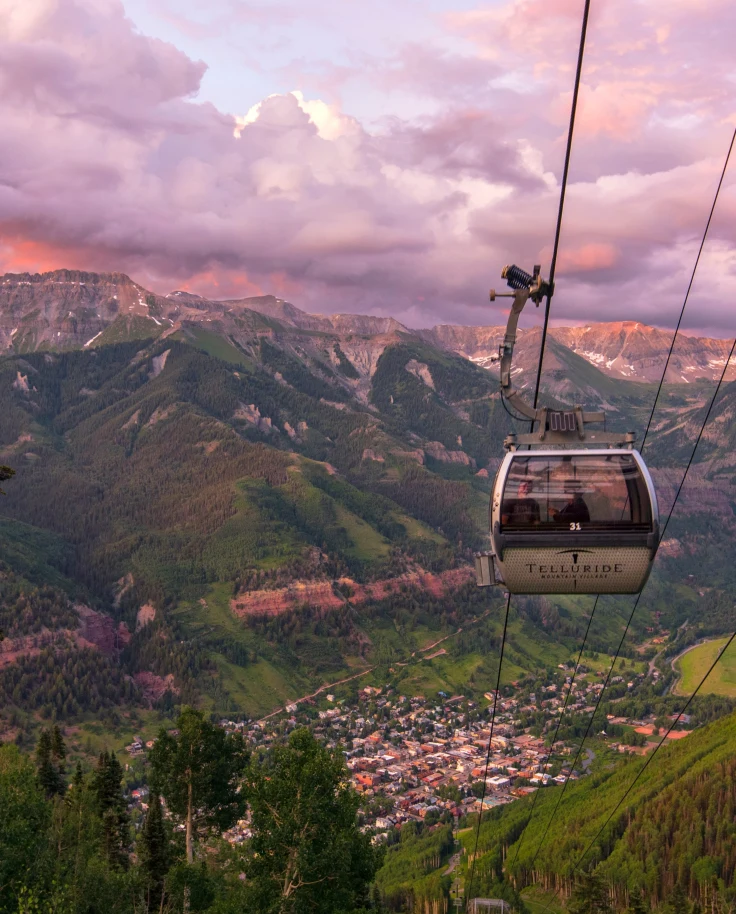 gondola going down a mountain with pink and purple skies, a great thing to do in the summer in Colorado