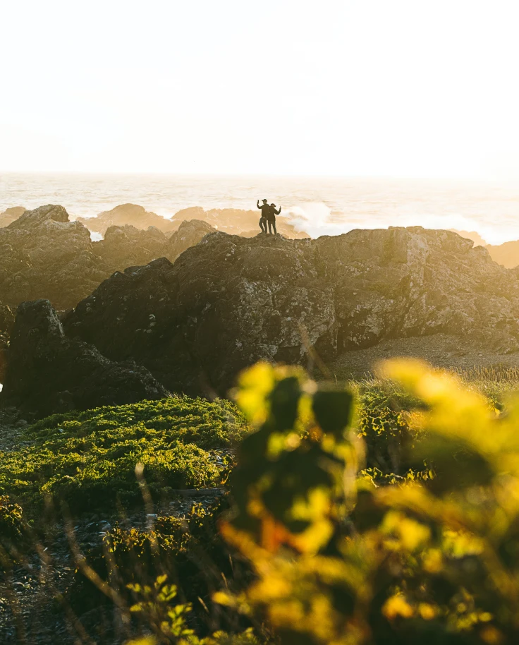 Two people standing on rocks at sunset.