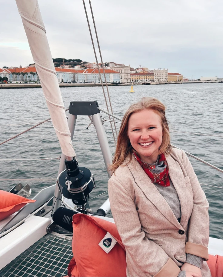 An individual sits on a sailboat, surrounded by water and buildings in the background.
