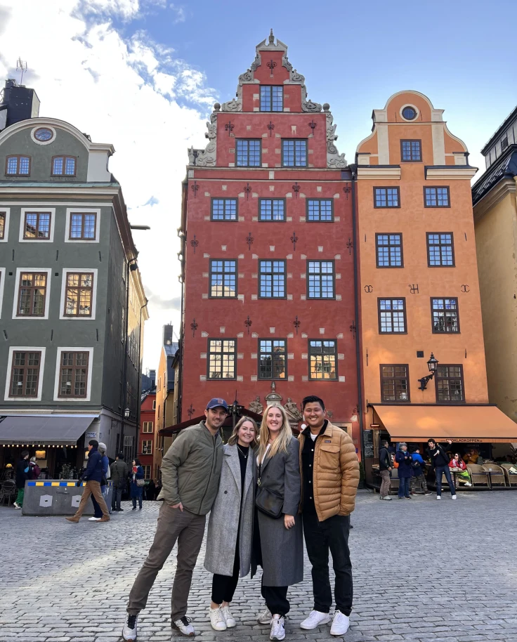 A group of people standing in front of colorful buildings on a street.