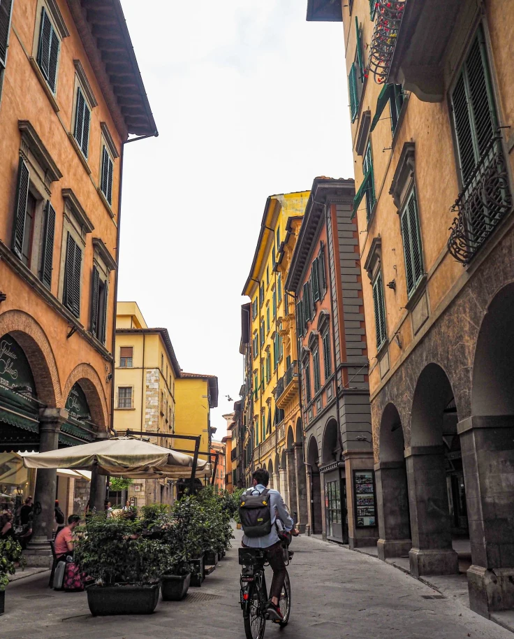 A person on a bicycle and people sitting on side walk in a street with buildings.