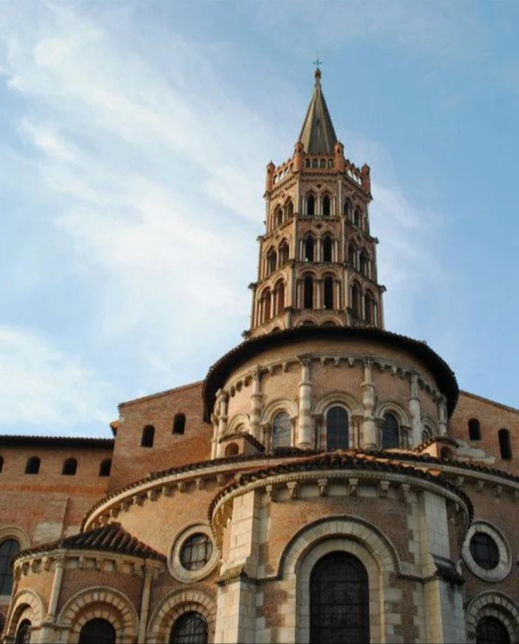 Historic brown building with cross at top against a clear sky and wisps of clouds.