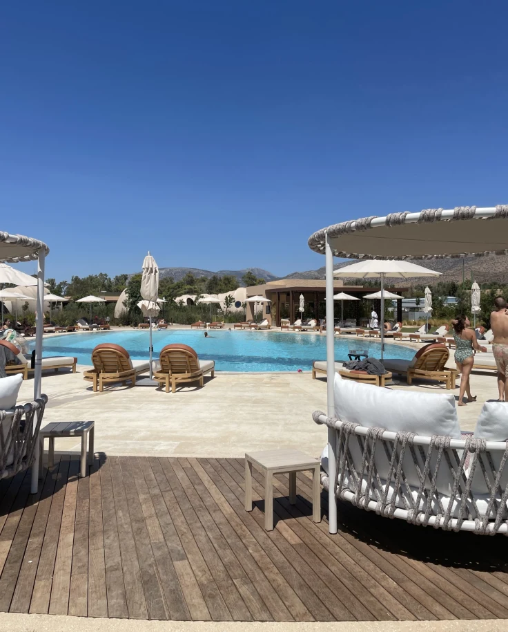 An outdoor pool area with sun loungers, umbrellas, and a clear blue sky suggests a leisure or vacation setting.