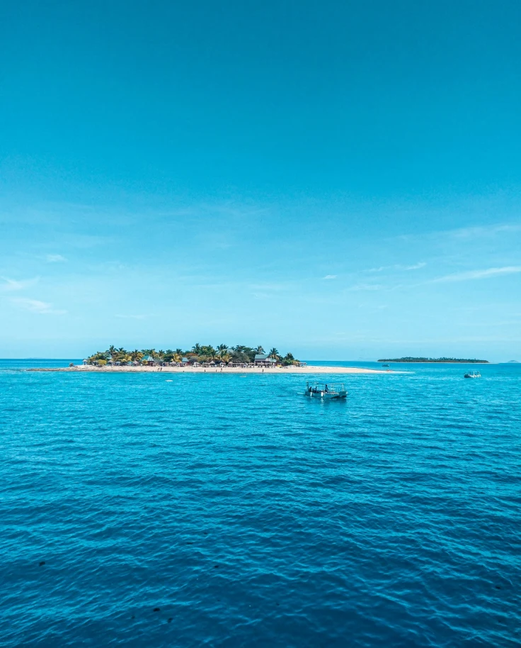 A tranquil tropical seascape with a boat on the water and an island in the distance, under a clear blue sky.