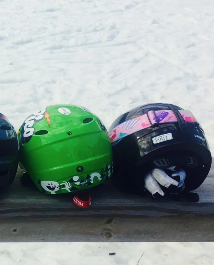 A picture of seven different colored ski helmets lined up on a wooden bench.