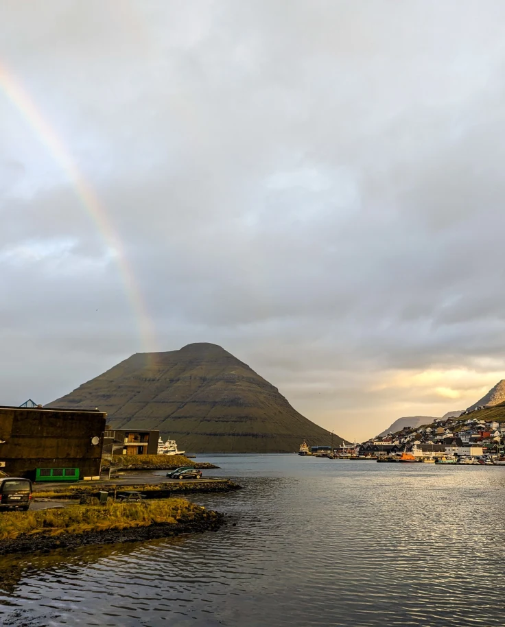 View of a river with a mountain in the background and rainbow in the cloudy sky