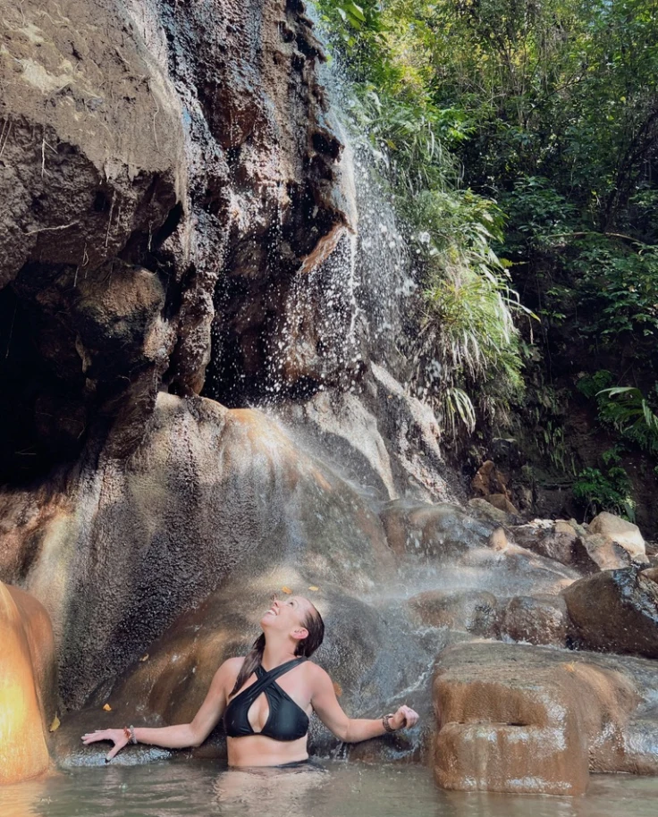A person standing in a natural pool of water next to a cliffside