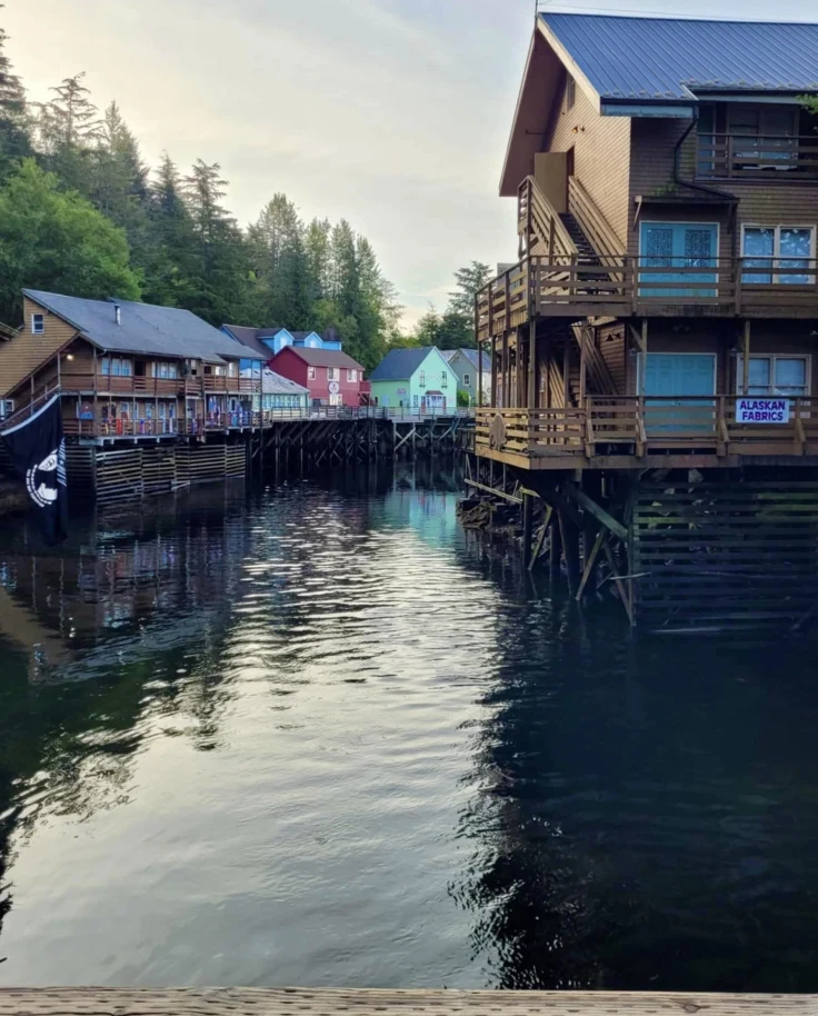 Brightly painted wooden buildings built over a body of water at Creek Street, Ketchikan at dusk.