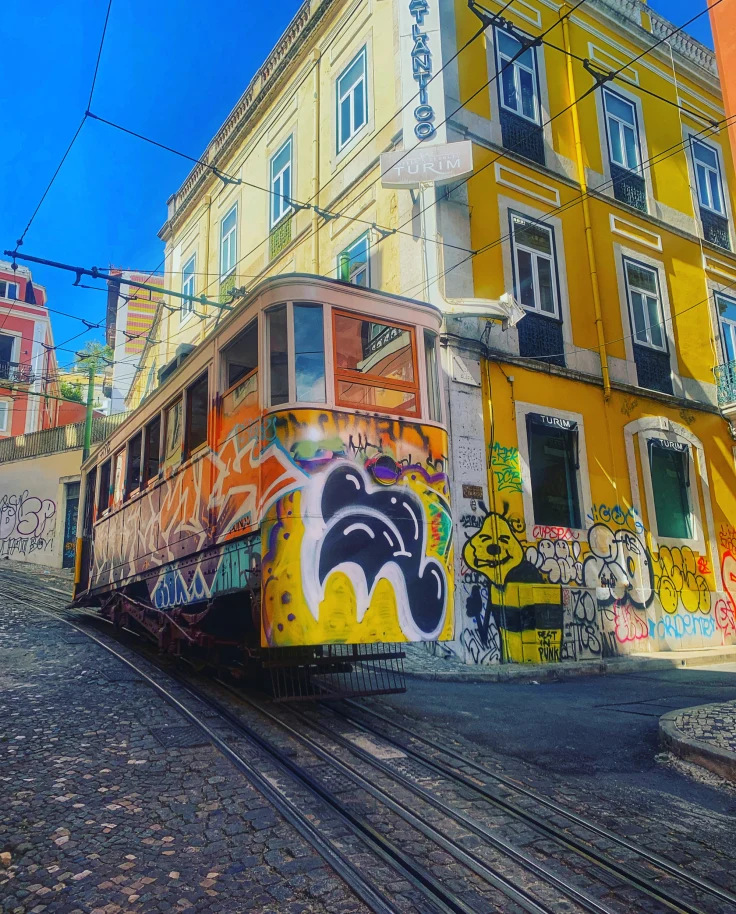 A yellow tram near a yellow building on the road during daytime.
