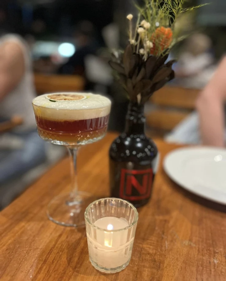 A sophisticated bar scene featuring a layered cocktail, fresh flowers, and the warm glow of candlelight.