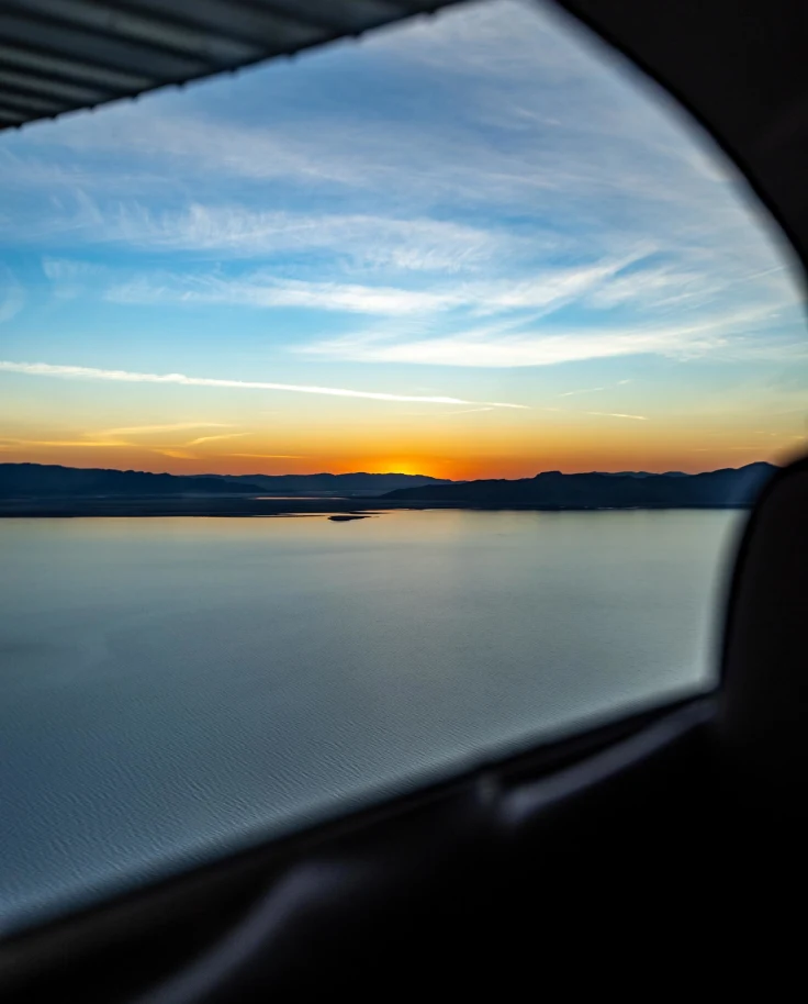 sunset over a pristine lake from the view of a car window