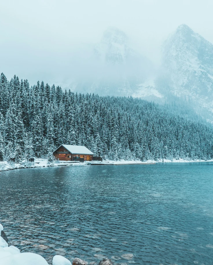 A brown wooden house near the water during daytime in the winter.
