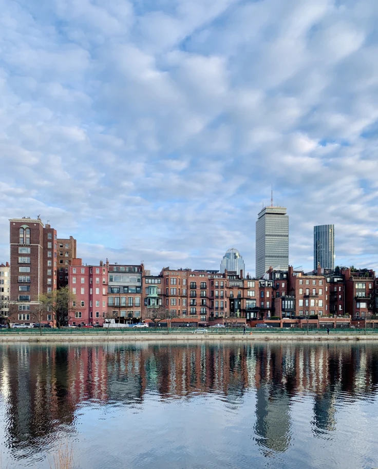 A view of the city from over the water with a cloudy sky overhead.