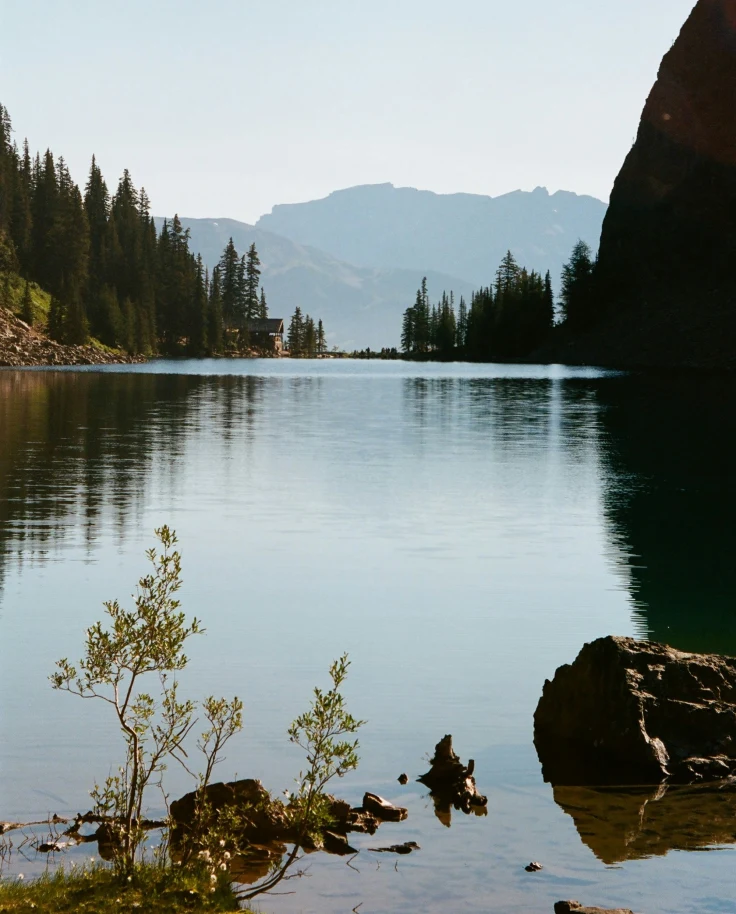 The image shows a mountain lake surrounded by trees and rocky terrain under a clear sky.