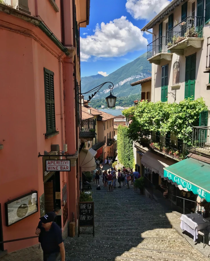 A charming street scene unfolds with vibrant buildings and a bustling square set against a mountainous backdrop.