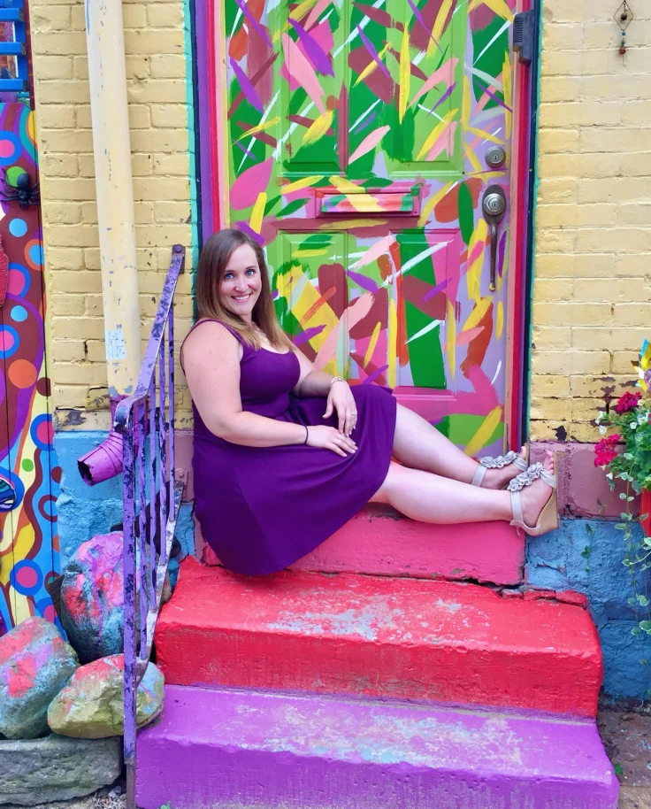 Advisor posing in purple dress sitting on red stairs in front of a colorful mural.