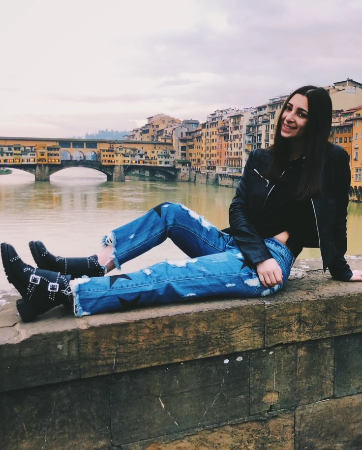 A woman in blue jeans and black jacket near city canal.