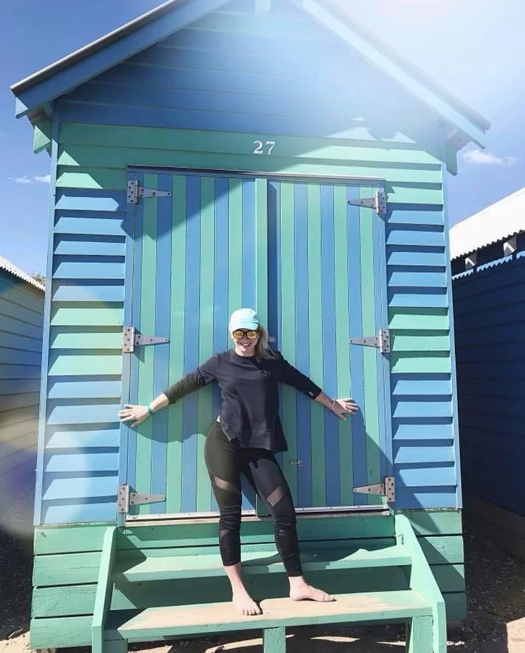 A woman posing in front of a blue green cabin.
