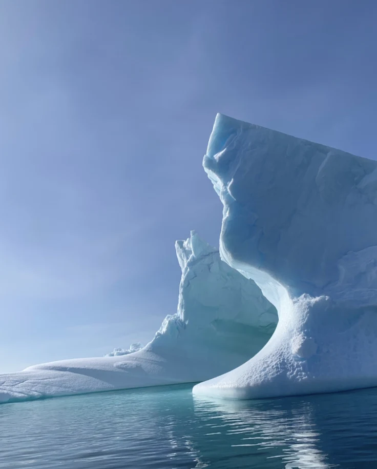 A view of a large ice berg and the turquoise blue water under a blue sky.