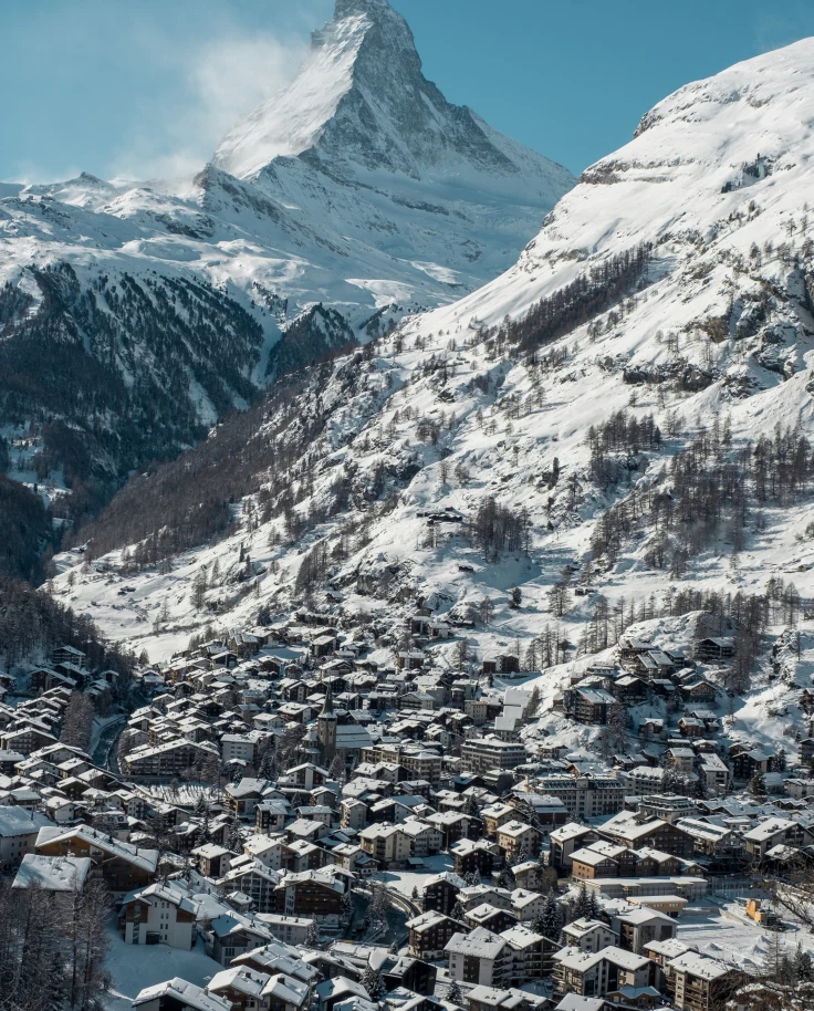 village in a valley surrounded by snowy mountains during daytime